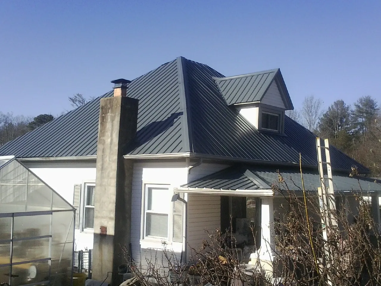 Dark blue standing seam metal roof on a white farmhouse with dormer — Slate & Tile Roof Repair by Roofing Brothers in Bumpus Mills