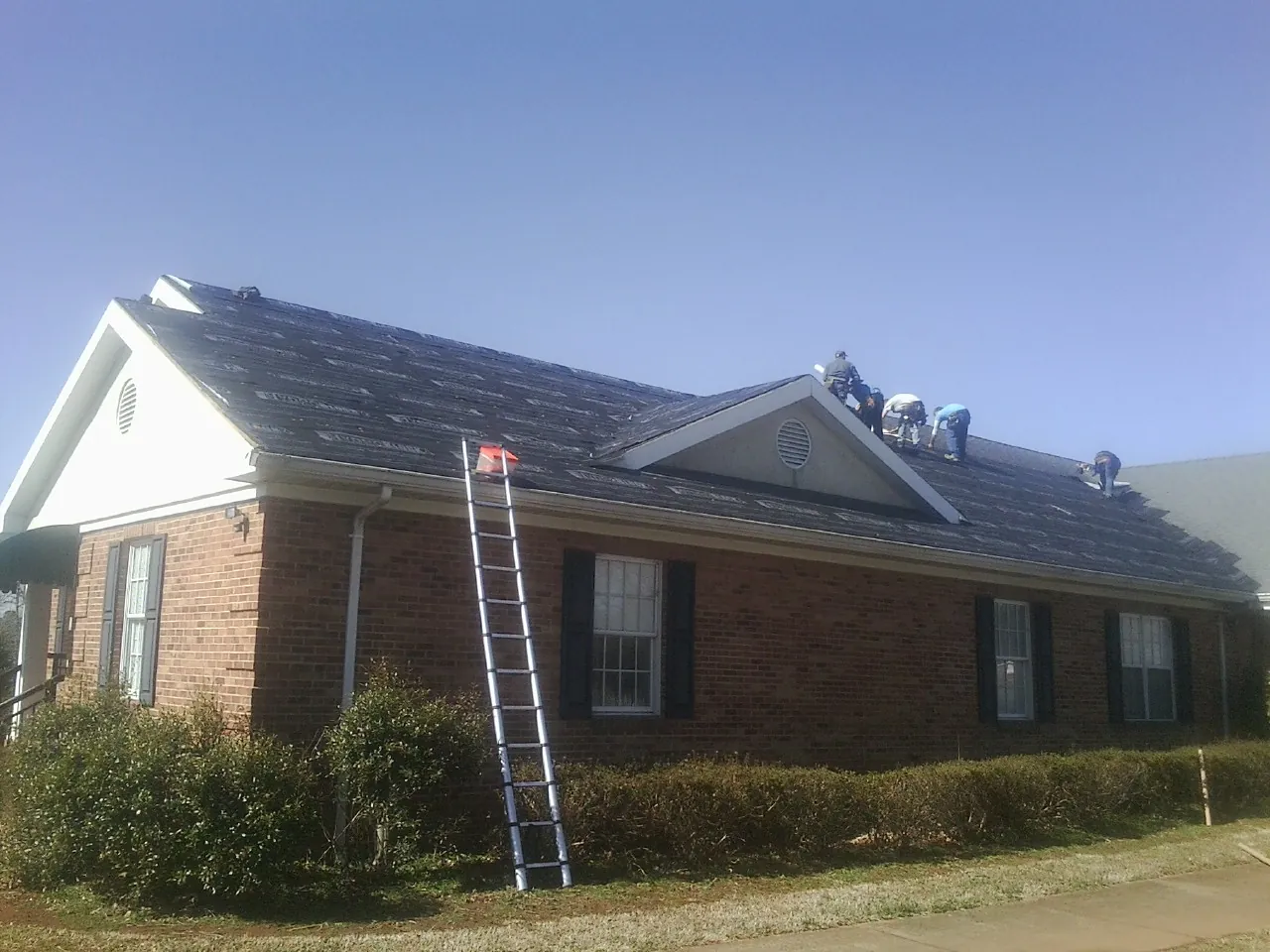 Crew tearing shingles off a brick ranch roof with a ladder set — Emergency Roof Repair work by our crew in Bumpus Mills
