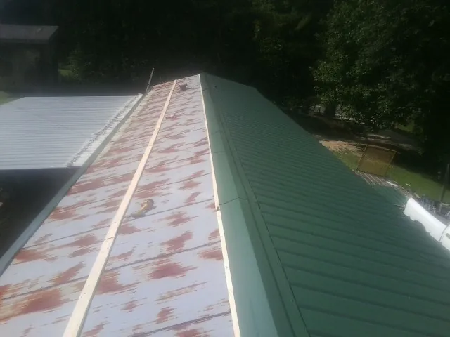 Old rusted panels beside newly installed green metal roofing — Wind Damage Roof Repair by Roofing Brothers in Bumpus Mills