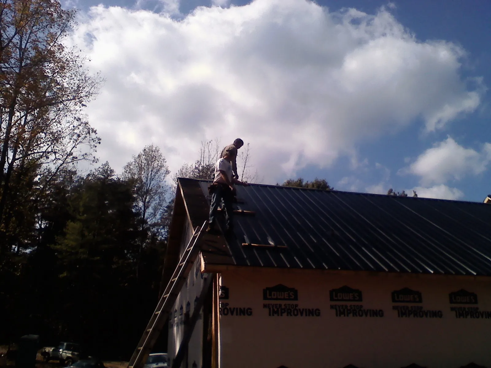 Roofer fastening dark metal panels high against a cloudy sky, from a Roof Inspection job in Bumpus Mills