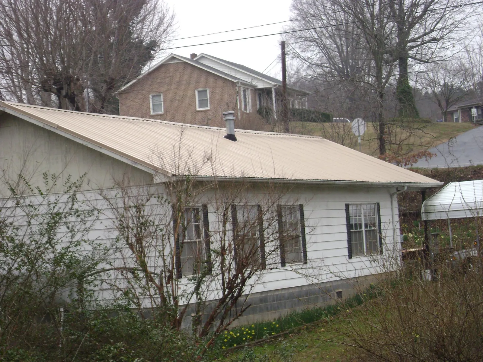 Tan metal roof on a white sided house set into a hillside — Commercial Roofing by Roofing Brothers in Bumpus Mills